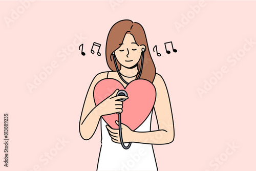 Woman listens to own heart using stethoscope to maintain spiritual harmony and psychological health. Positive girl with big heart takes care of cardio organs for improve well-being.