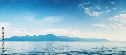 A serene summer seascape with clear water and beautiful blue sky adorned with white clouds Mountain silhouettes appear on the hazy horizon enhancing the tranquility and serenity of the ocean The imag