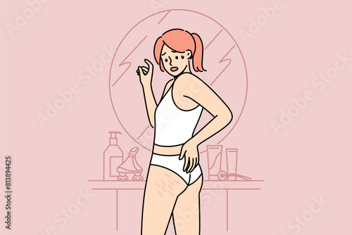 Woman sees cellulite on butt and thighs standing near mirror, and needs consult trainer to combat excess weight. Cellulite causes fear in girls, want to lose weight or improve own body