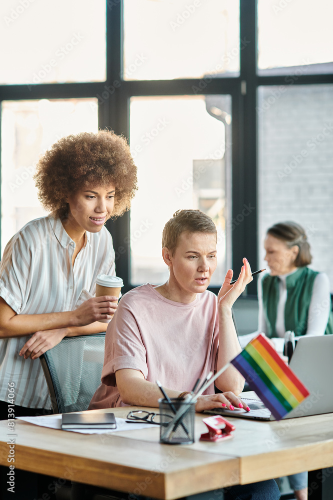Obraz premium Devoted diverse businesswomen working together on project in office, pride flag.