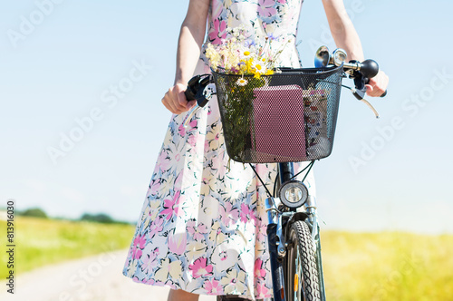 Wild flowers bouquet carried by young woman in dress with flowers in bicycle basket , flowers  gathered in a meadow  by woman in the countryside in summer time sunny day