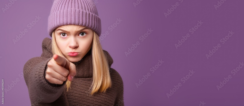 Unhappy teenager blonde girl with a winter hat pointing to the side against a purple isolated background with copy space image Unhappy teenager blonde girl with a winter hat pointing to the side against a purple isolated background with copy space image