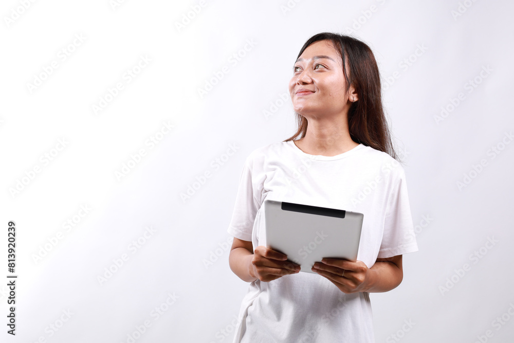 Smiling young asian college student woman using tablet computer, happy student woman in casual looking empty space standing over white background Smiling young asian college student woman using tablet computer, happy student woman in casual looking empty space standing over white background