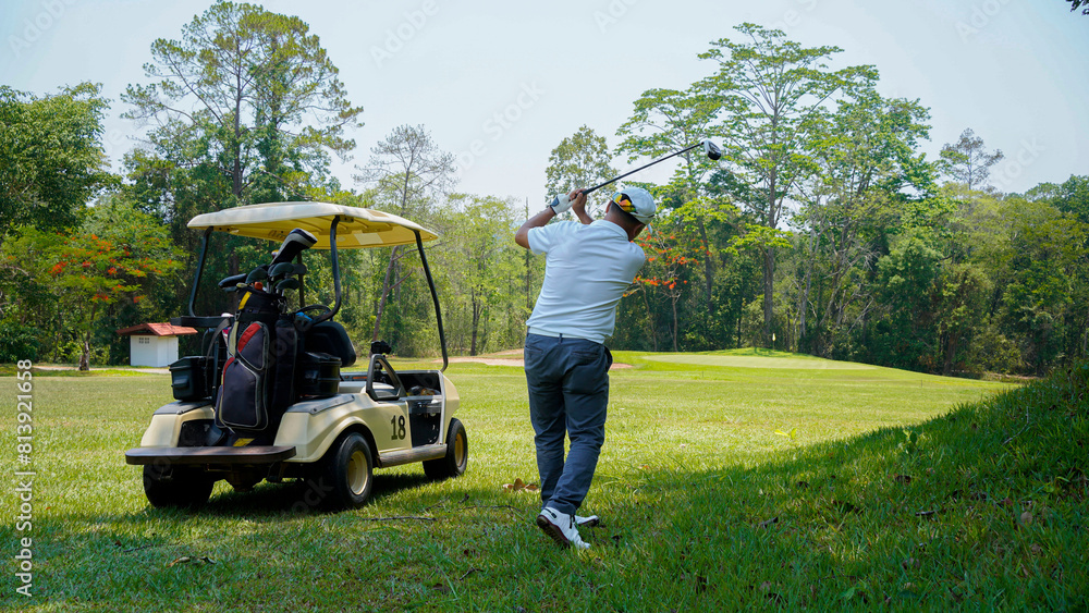 Golfer plays golf on the fairway with golf cart in the evening at sunset background.