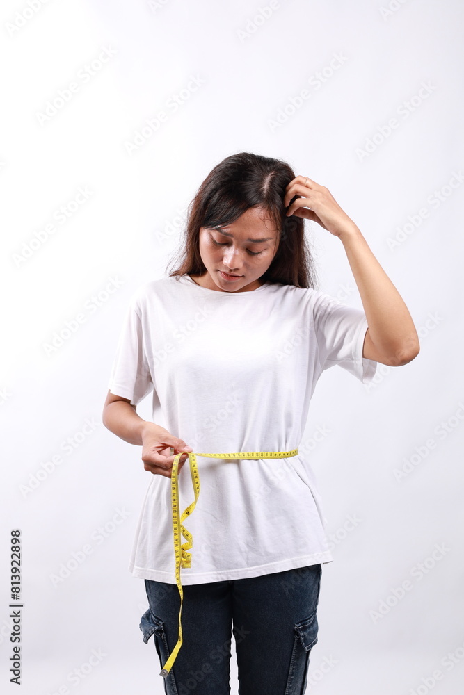 Young sad confused woman wears blue clothes hold measuring tape on waist spread hand isolated on white background. Proper nutrition healthy fast food unhealthy choice concept Young sad confused woman wears blue clothes hold measuring tape on waist spread hand isolated on white background. Proper nutrition healthy fast food unhealthy choice concept