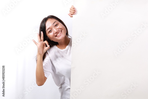 Happy smiling beautiful young woman showing blank signboard or copyspace for slogan or text while making okay hand gesture, isolated over white background