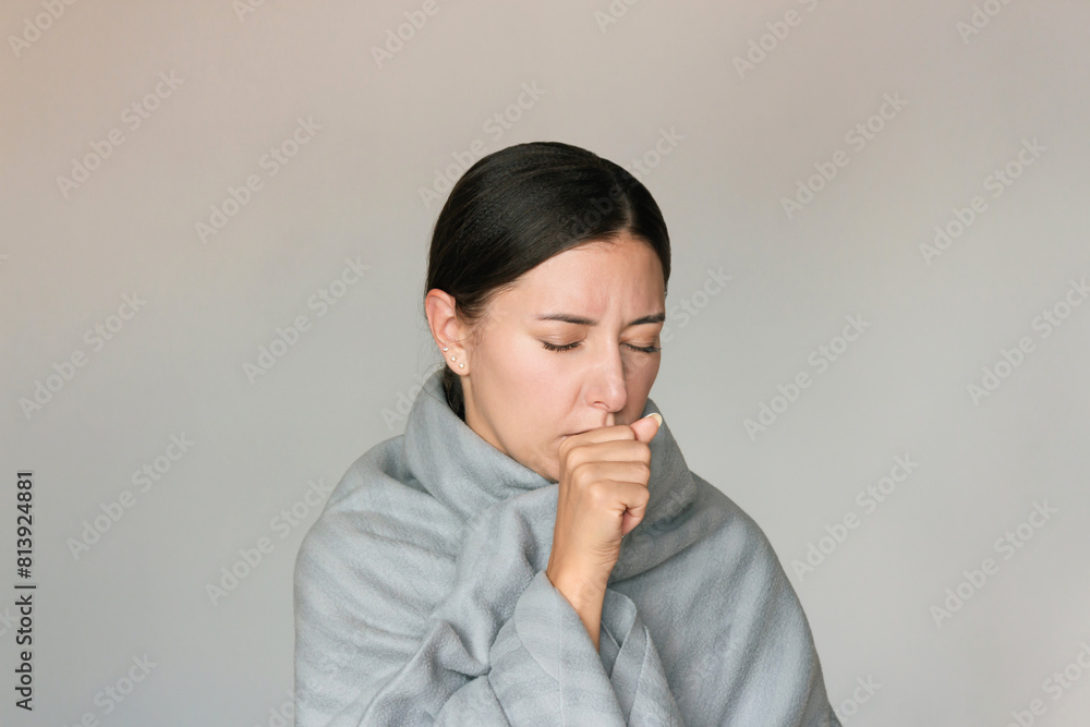 A young pretty Caucasian brunette woman, covered with a gray plaid, suffers from a cold, coughs with his eyes closed. The epidemic of flu and colds. Complications after the disease. A young pretty Caucasian brunette woman, covered with a gray plaid, suffers from a cold, coughs with his eyes closed. The epidemic of flu and colds. Complications after the disease.
