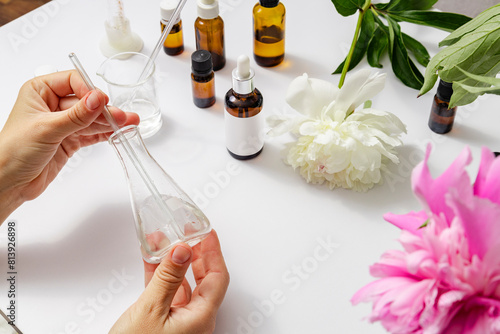 Woman holding lab flask during experimenting of production of peony oils, perfume and cosmetics