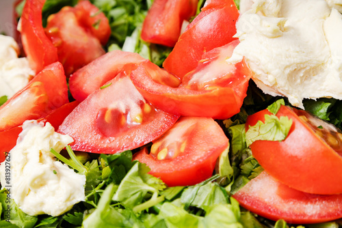 Closeup of slices of tomatoes, fresh chopped lettuce and fat cream as dressing