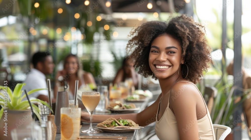 A joyful young woman laughs while eating at a restaurant, a plate of food and drinks in front of her. A joyful young woman laughs while eating at a restaurant, a plate of food and drinks in front of her.
