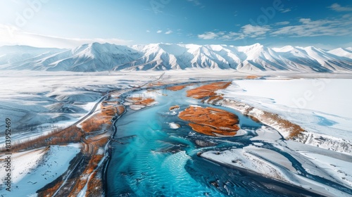 Aerial view of a winding highway through snow-capped mountains with a river and blue skies.