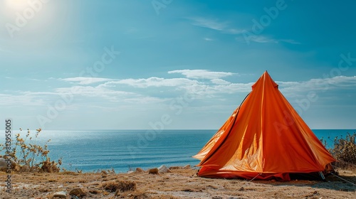 An orange tent pitched on a field with a view of the sea and blue sky on a sunny day.