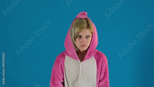 Female teenager gesticulates touching face with hand expressing fatigue. Tired girl in pajamas makes finger gun gesture on blue background photo