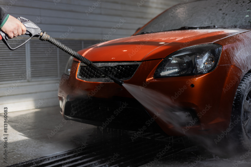 A man washes his car by spraying it with water from a pistol. The man took his car to the car wash to wash it of dirt after the road. A man washes his car.