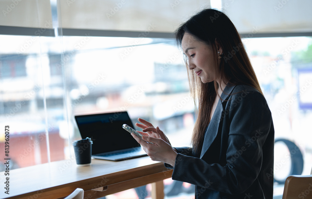 Fototapeta premium Asian young beautiful happy professional successful businesswoman designer sitting smiling at workstation desk using laptop notebook computer and smartphone working remotely online at home office