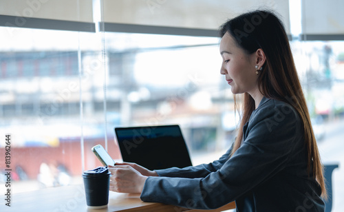 Asian young beautiful happy professional successful businesswoman designer sitting smiling at workstation desk using laptop notebook computer and smartphone working remotely online at home office