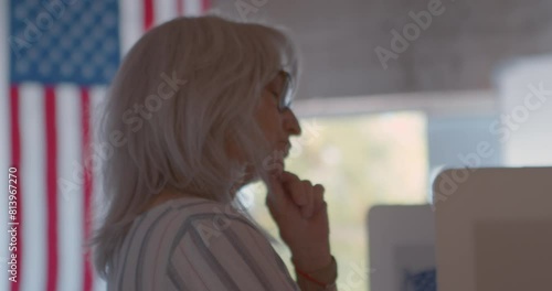Mature woman voting at a polling station with another female voter in the background.