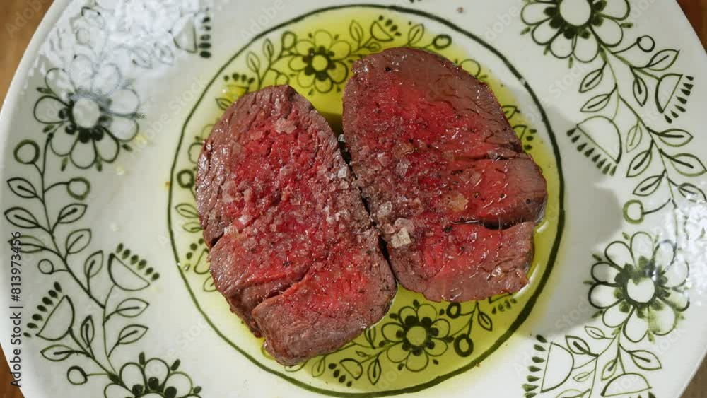 View from above on two slices of medium rare beef served with oil and seasonings on ceramic patterned plate. Juicy meat with bloody centre ready to eat and served on wooden table of luxury restaurant. View from above on two slices of medium rare beef served with oil and seasonings on ceramic patterned plate. Juicy meat with bloody centre ready to eat and served on wooden table of luxury restaurant.