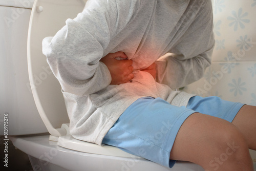 Man sitting on toilet and holding his stomach with stomach pain causes of gastritis or constipation with red dot in bathroom and sunlight blurred background concept of medical and health problems.
