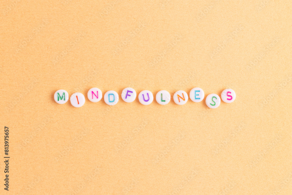 Mindfulness. Word made of white round beads with multicolored letters on a gold colored background. Mindfulness. Word made of white round beads with multicolored letters on a gold colored background.