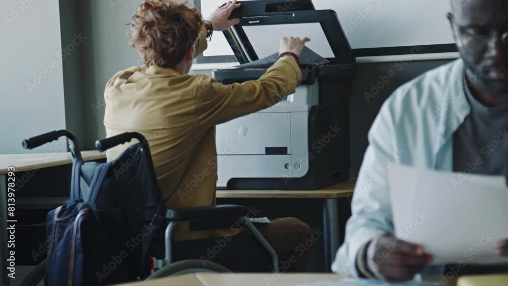 Young man in wheelchair using printer to copy business papers while working in office Young man in wheelchair using printer to copy business papers while working in office