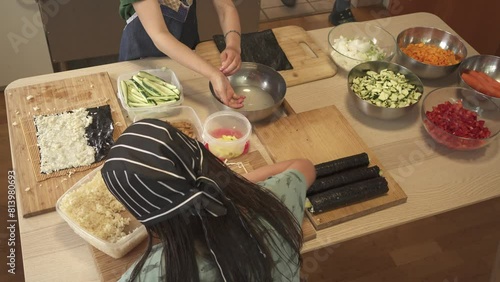 zenithal view video of girls making sushi maquis, dressed in aprons and cooking hats, wooden boards and vols with prepared vegetarian ingredients. photo