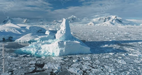 Aerial view panorama massive iceberg floating frozen ocean in Antarctica. Majestic winter Antarctic glacier melting under sun. Snow covered mountains blue cloudy sky. Global warming and climate change