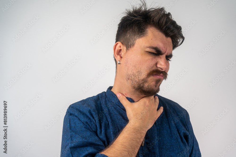 Obraz premium Young sick man having sore throat, looking at copy space over grey studio background. Bearded man touching his neck, suffering from throat disorder, tonsillitis, throat cancer, cold