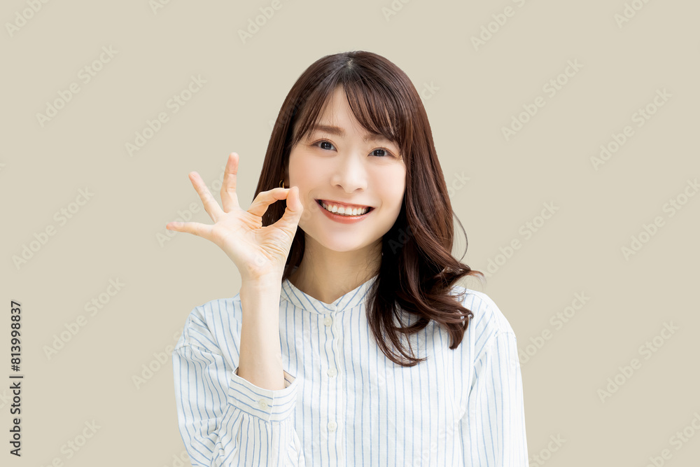 OKポーズをする笑顔の女性_ベージュ OKポーズをする笑顔の女性_ベージュ