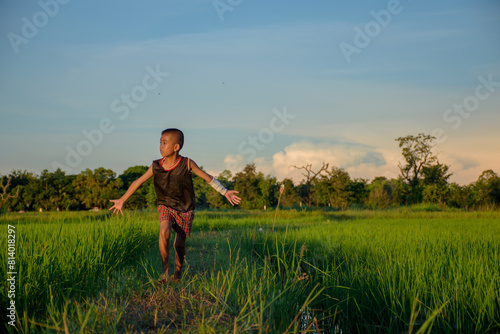 Asian young boy with wounds and bandages on the arms and heads running joyfully in the rice fields in the evening sunset on the background of a warm sky.
