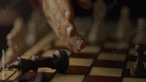 Overthrow of the king chess piece. A young experienced player knocks over a chess piece onto the board demonstrating victory. Close-up of a chess player's hand knocking over a king piece photo