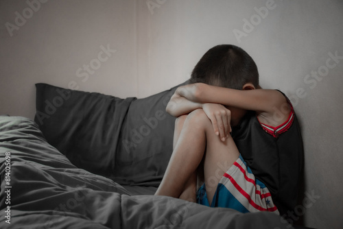Side view of a boy sitting on a bed scared and unhappy from depression due to family problems in dark tone background. Children who are depressed and suffering from domestic violence.
