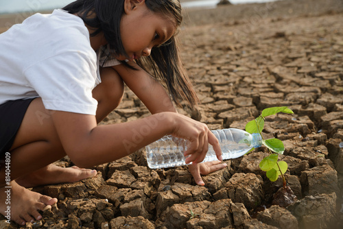 Asian girl planting tree and watering seedling on dry and crack ground to restore and change earth and environment. Drought and El Niño condition concept.