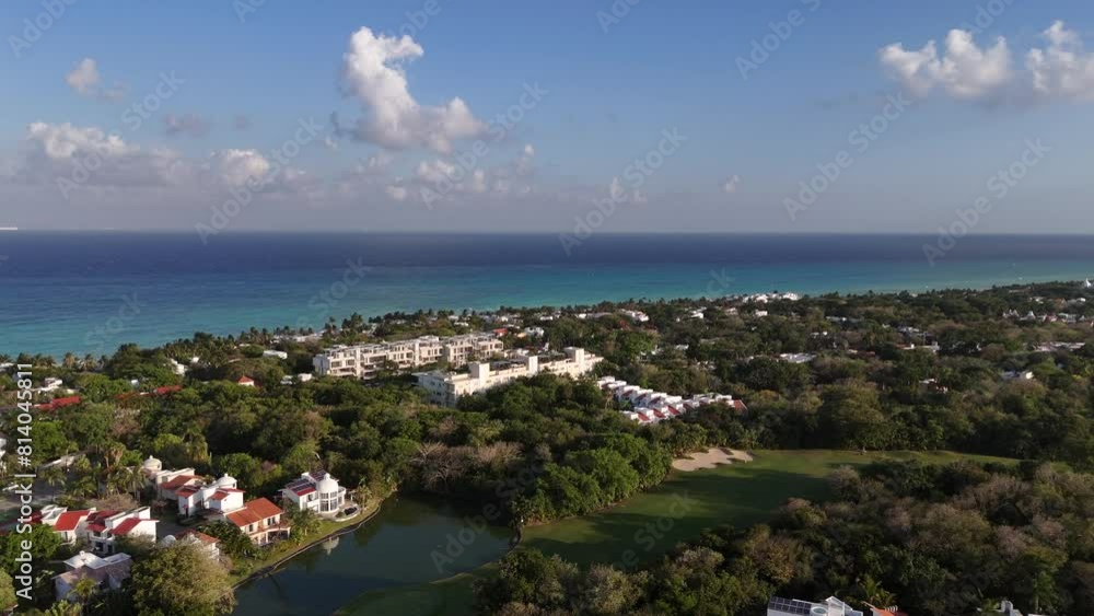 Aerial drone view of buildings surrounded by tropical green forest and blue Caribbean Sea on the background with beautiful blue sky and few clouds on a sunny afternoon in Mexico Aerial drone view of buildings surrounded by tropical green forest and blue Caribbean Sea on the background with beautiful blue sky and few clouds on a sunny afternoon in Mexico