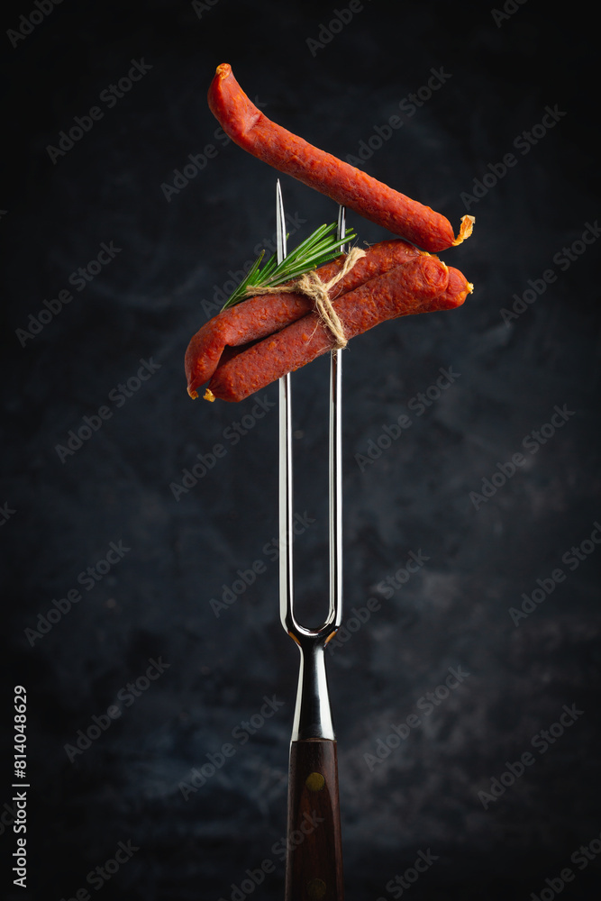 Dried pork sausages on a metal fork. Kabanos Close up on a black background. Dried pork sausages on a metal fork. Kabanos Close up on a black background.