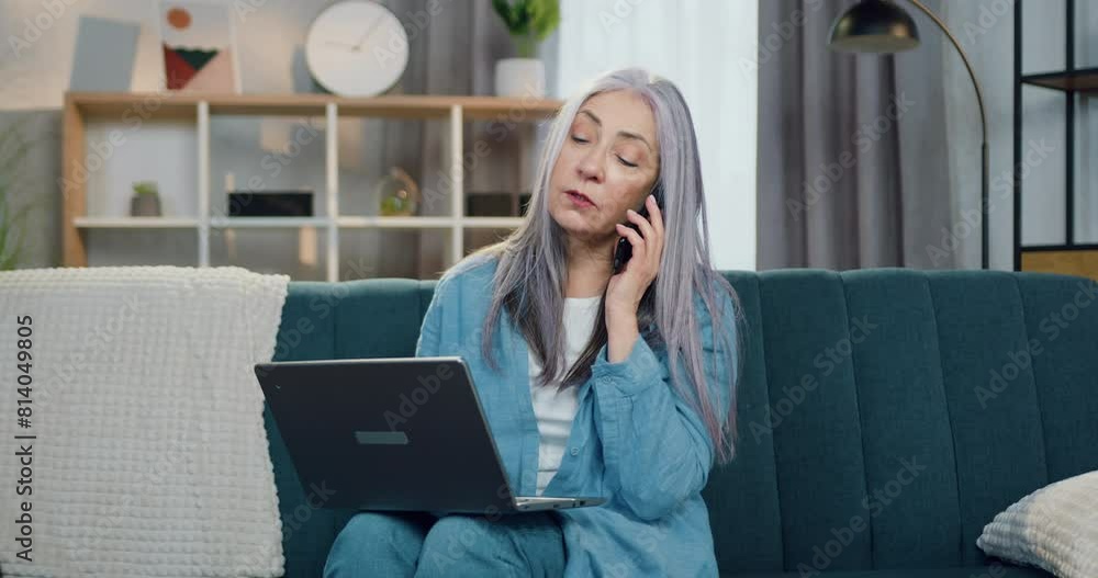 Portrait of mature woman talking on mobile and working on laptop which on contemporary living-room background Portrait of mature woman talking on mobile and working on laptop which on contemporary living-room background
