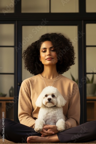 A woman in her 30s practicing mindfulness and meditation in a serene pet-friendly yoga studio, surrounded by tranquil vibes and her loyal Bichon Frise photo