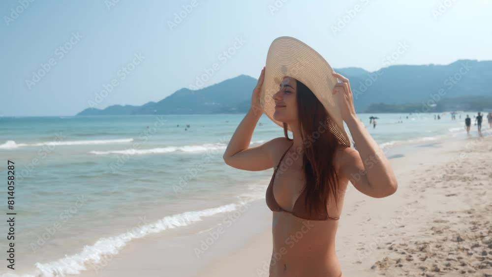 Woman in bikini, large hat enjoys beach holiday shore warm ocean. Face is illuminated with of happiness and carefreeness. Happiness overwhelms, woman bathes in rays of sun and enjoys moment happiness.