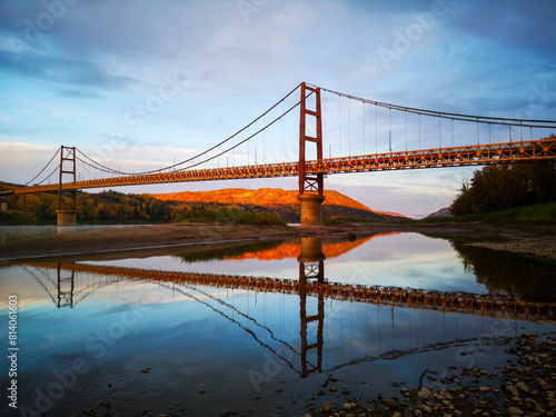 Dunvegan Bridge with reflection on the peaceful Peace River in the early sunrise with a blue sky in the background in Northern Alberta, Canada