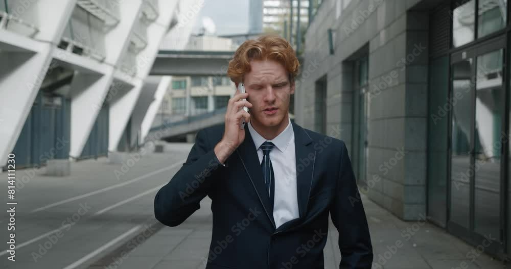 Young handsome businessman is having active conversation on phone on city street. Red-haired man actively waves his hands during call. Intensity of emotions during active decision making in business. Young handsome businessman is having active conversation on phone on city street. Red-haired man actively waves his hands during call. Intensity of emotions during active decision making in business.