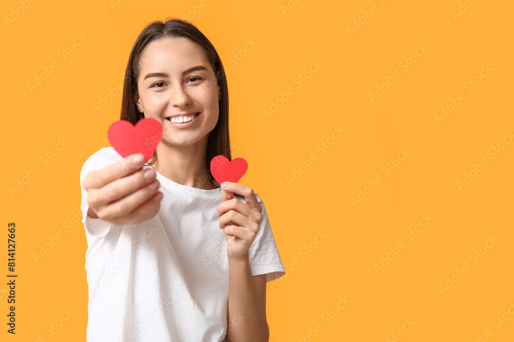 Beautiful young woman with paper hearts on yellow background