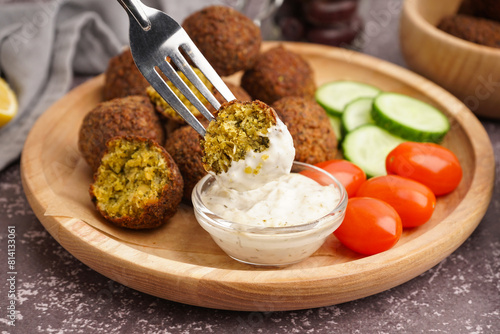 Fork with delicious falafel balls, sauce and vegetables on grunge background, closeup