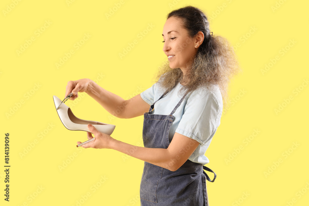 Female shoemaker measuring high-heeled shoe on yellow background Female shoemaker measuring high-heeled shoe on yellow background