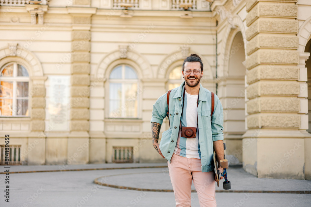 Fototapeta premium Portrait of hipster standing on city street with skateboard in hands.