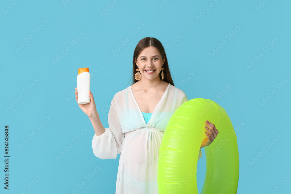 Beautiful young pregnant woman with bottle of sunscreen cream and inflatable ring on blue background Beautiful young pregnant woman with bottle of sunscreen cream and inflatable ring on blue background