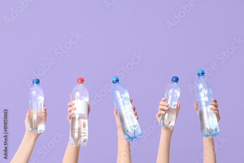 Female hands with different bottles of water on lilac background