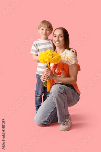 Happy woman and her little son with bouquet of beautiful narcissus on pink background
