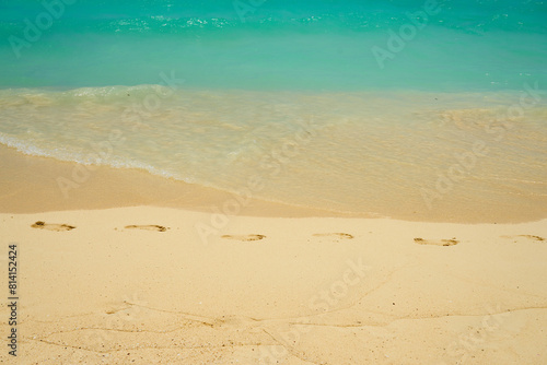 Waves and foam on a tropical sandy beach with footprints on sand