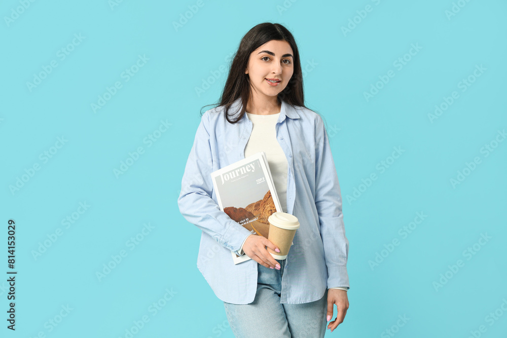 Fototapeta premium Beautiful young happy woman with magazine and cup of coffee on blue background