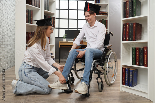 Female graduate helping her classmate in wheelchair at library photo